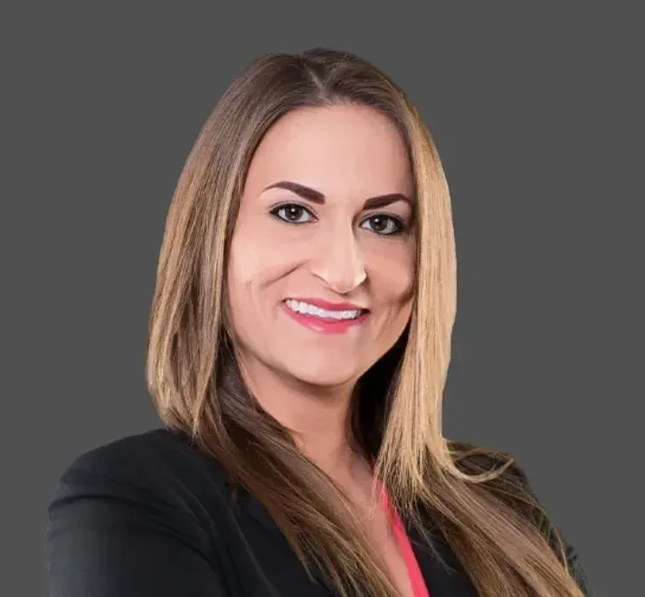 Smiling woman in business attire on a gray background, professional headshot.