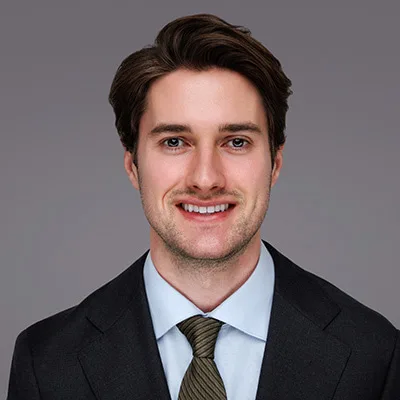 A suitable alt text could be: Smiling person in a suit and tie against a