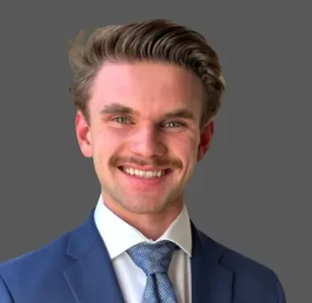 Portrait of a smiling man in a suit and tie against a gray background.