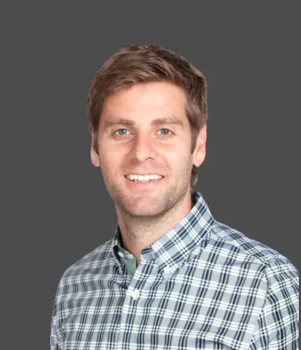 Man smiling in plaid shirt against a gray background.