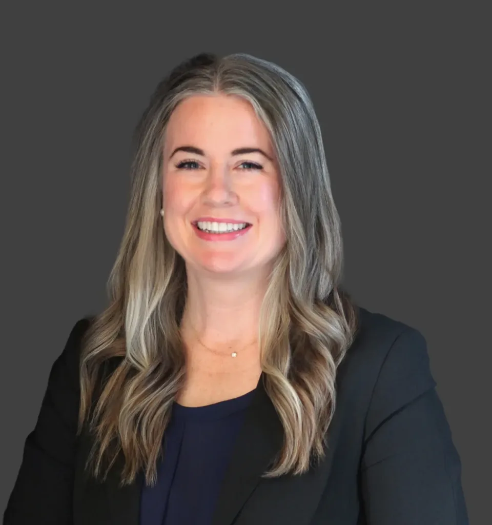 Smiling woman with long hair in a black blazer, neutral background. Professional portrait.