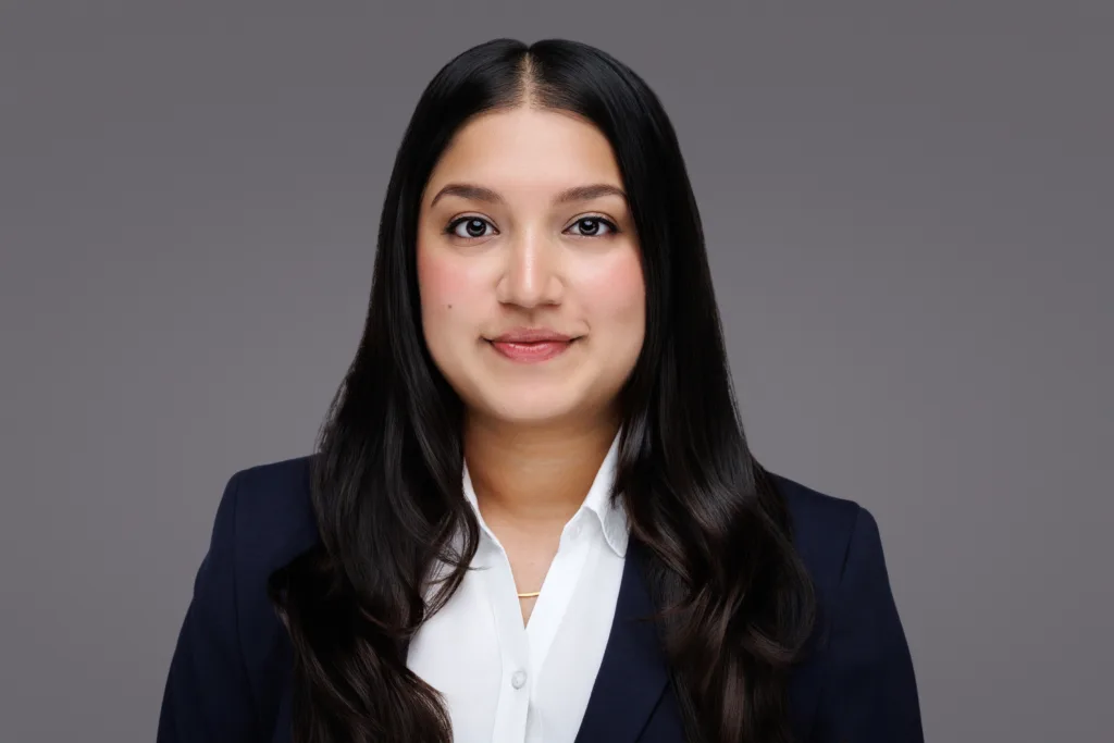Business professional woman with long black hair in a navy blazer and white shirt, smiling in a portrait.